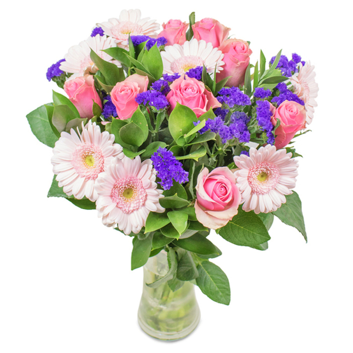 This eye-catching floral arrangement, composed just steps from Harlesden's vibrant Park Parade, features an inviting medley that celebrates both tradition and artistic flair. The bouquet centers on a cluster of seven to nine pink roses-some tight in spiral elegance, others softly unfurling-each petal alive with shades ranging from blush to deeper rose. These are complemented by approximately five to seven pale pink gerbera daisies, their broad, ruffled heads radiating pastel petals around nearly white centers that glimmer in soft light. Between the main blooms, vivid clusters of purple statice provide a striking pop of color and intriguing texture, reminiscent of wildflowers found around Harlesden's Roundwood Park. A base of lush, emerald foliage imparts abundance and freshness-each leaf vivid and crisp, echoing the greenery glimpsed in local front gardens. Arranged in a slender, transparent vase where stems and water catch and reflect the light, the bouquet conjures the feel of a fresh flower delivery, ideal for birthdays, anniversaries, Mother's Day, or simply as a heartening decor accent. Florist Harlesden ensures every detail is considered, making this bouquet a memorable gift or personal treat for homes and offices throughout the community-from Craven Park to Harlesden Gardens-conveying joy, celebration, and deep affection in every exquisite bloom.