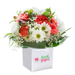 Brimming with the uplifting energy of springtime in Harlesden, this bouquet offers a joyful mix of colour, fragrance, and form-all expertly cradled in a smart white gift bag. The rich coral and red carnations take center stage, their ruffled petals layered like delicate fabric, promising both vibrancy and tender sentiment. Interspersed among them, the white daisies bring sheer cheer, their sunny green centers reminiscent of pocket parks blooming throughout Harlesden. Wispy sprigs of baby's breath weave an ethereal softness, imbuing the bouquet with lightness and innocence. A few closed purple-tinted buds, set off to one side, lend a sense of graceful anticipation-echoing the neighbourhood's creative energy and its ever-changing streets. Deep, glossy green leaves anchor the composition, forming a broad collar that grounds the flowers and frames their beauty with natural grandeur. Confidently arranged and presented with sturdy white ribbon handles, the bouquet is captured against a pure white background to show off each detail. Whether destined for a birthday, an anniversary, or simply to lift someone's spirits in Harlesden, this bouquet is a testament to the skill, care, and friendliness of local florists-a true floral embrace from the heart of the community.